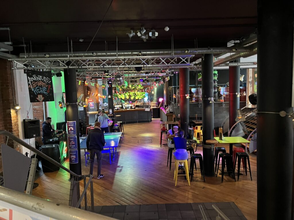 Colorful and lively hotel bar and game lounge with ping pong tables, neon lighting, and eclectic decor. Highlights the fun social spaces available at some dog friendly hotels in Dublin.