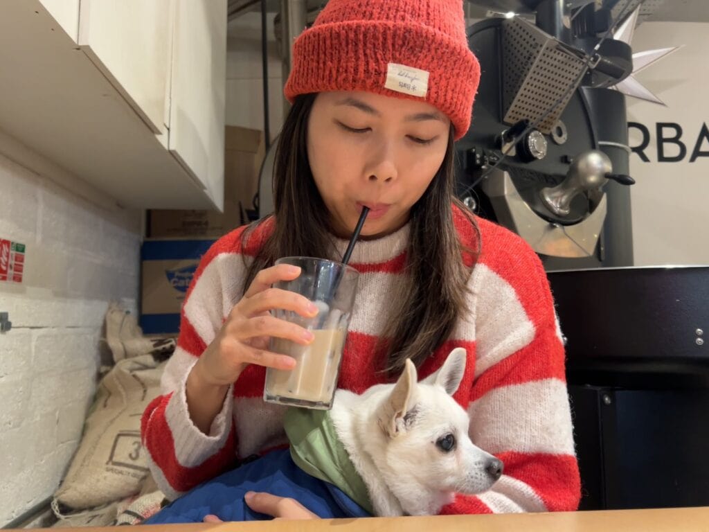 Woman in a red and white striped sweater sipping an iced latte through a black straw while holding a small white dog.
