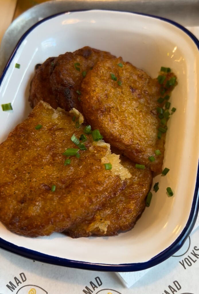Close-up of crispy golden potato pancakes garnished with chopped chives, served in a white enamel dish.